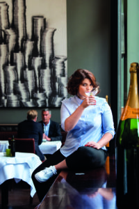 Autorin Sophie Passmann sitzt in einem Café mit einem Glas in der Hand.