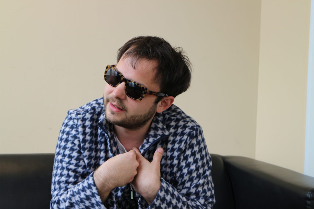 Peter Horazdoysky von der Band Bilderbuch sitzt in seiner Garderobe und trägt eine Sonnenbrille.