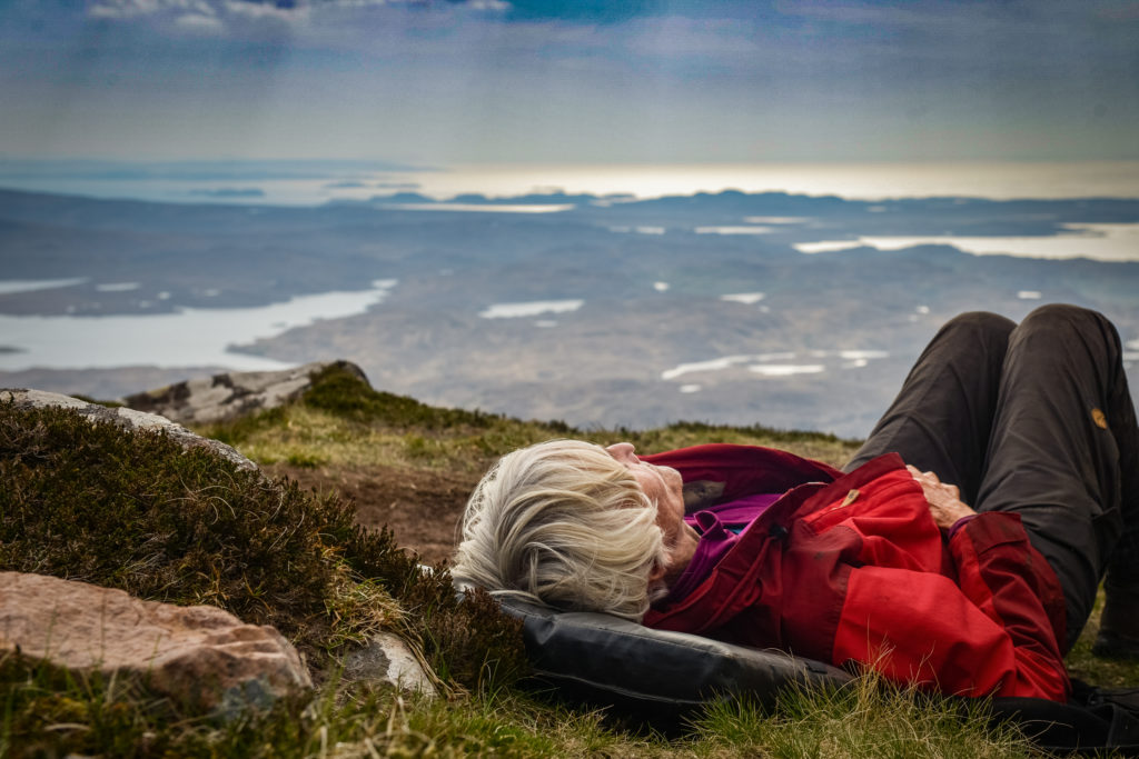 Eine Frau liegt auf der Kuppe eines Berges und schaut in den Himmel