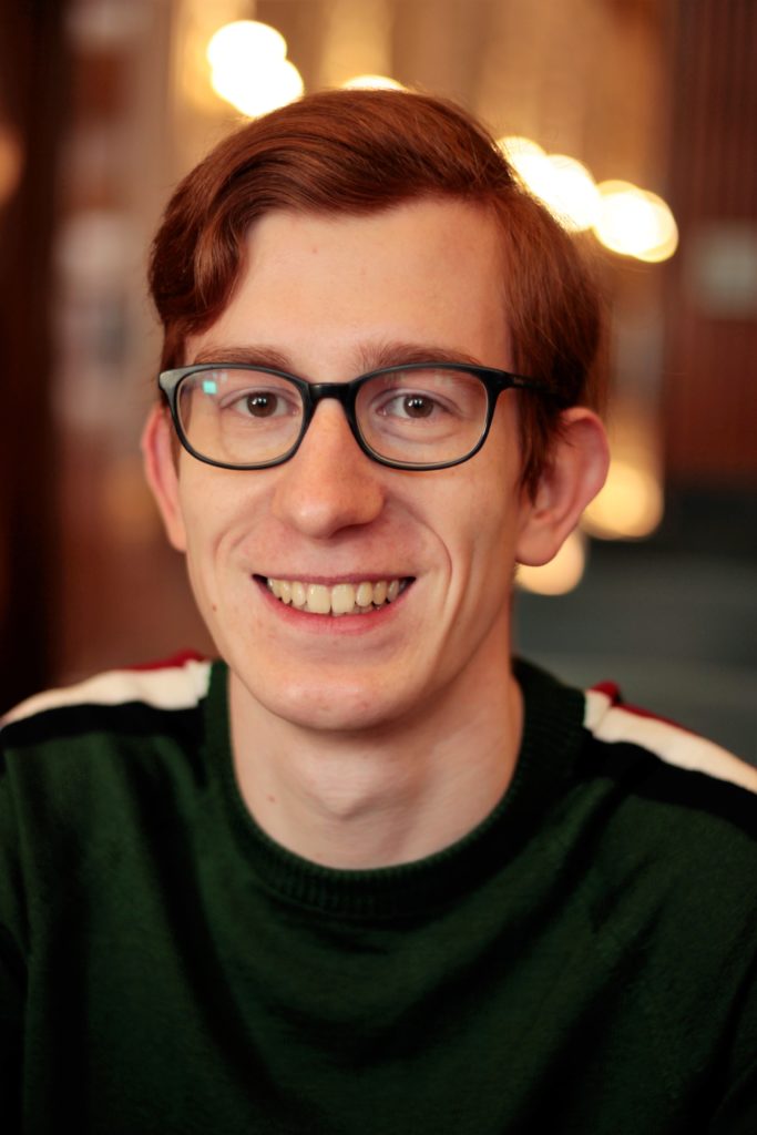 Ein junger Mann mit rötlichen Haaren und Brille.